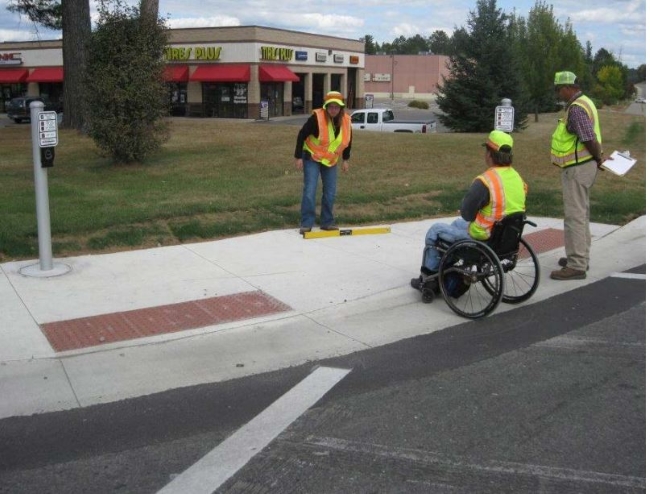 Three people inspecting a curb ramp at a street intersection